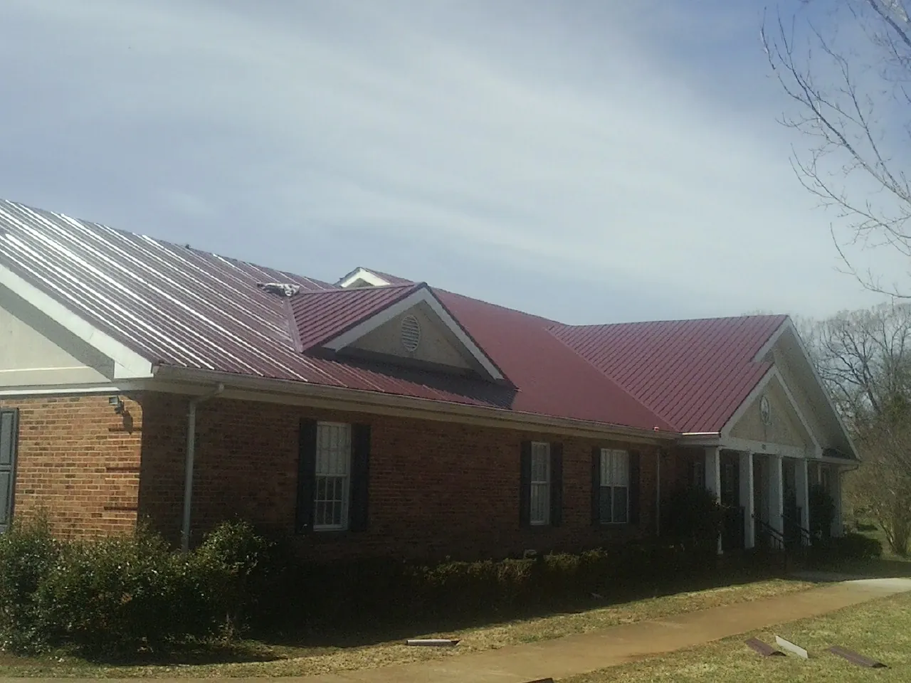 Red metal roof with gabled entries on a long brick building, from a Hail Damage Roof Repair job in Mount Morris